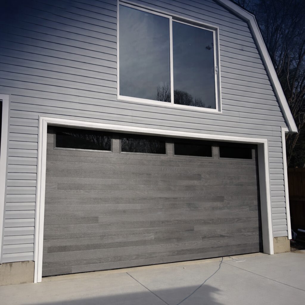 Modern gray garage door on a white house exterior.