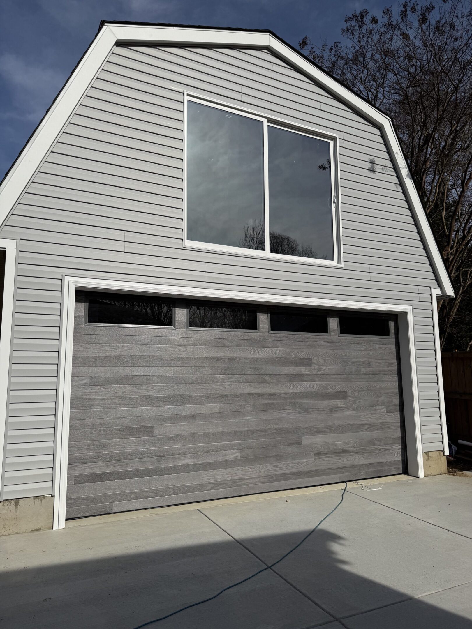Modern gray garage door on a two-story house with siding.