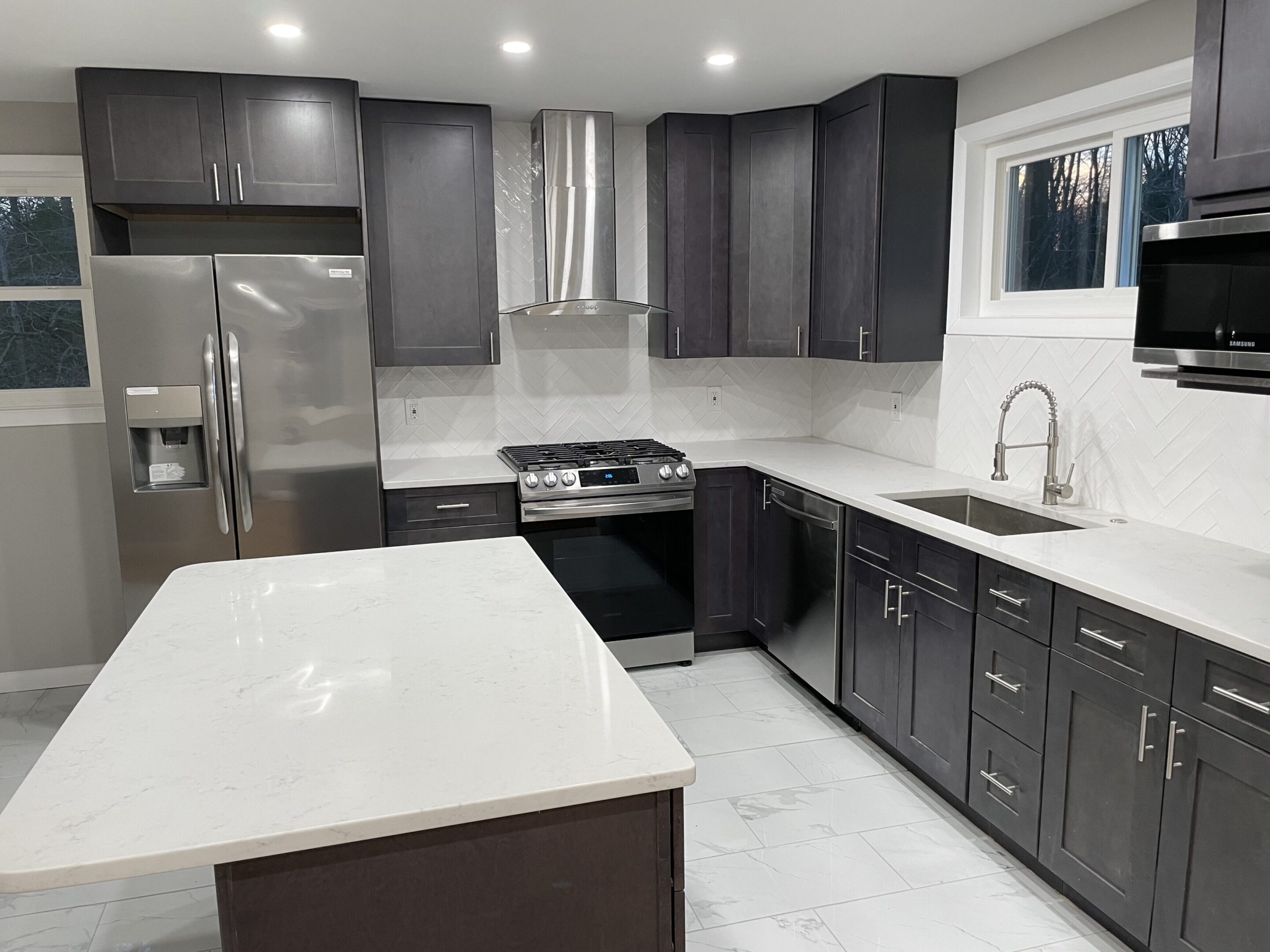 Modern kitchen with dark cabinets and white countertops.