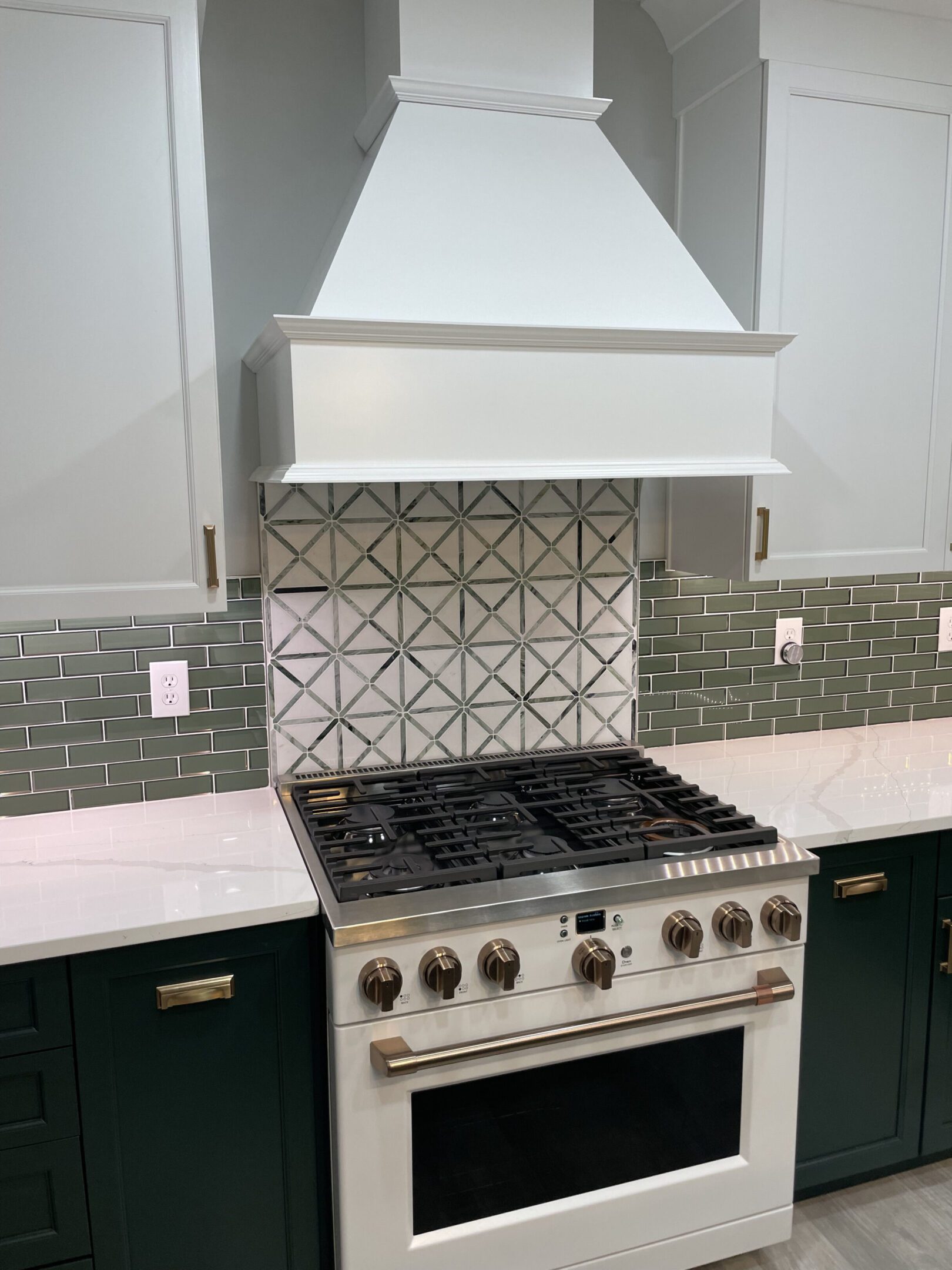 Modern kitchen stove with white range hood and green backsplash.