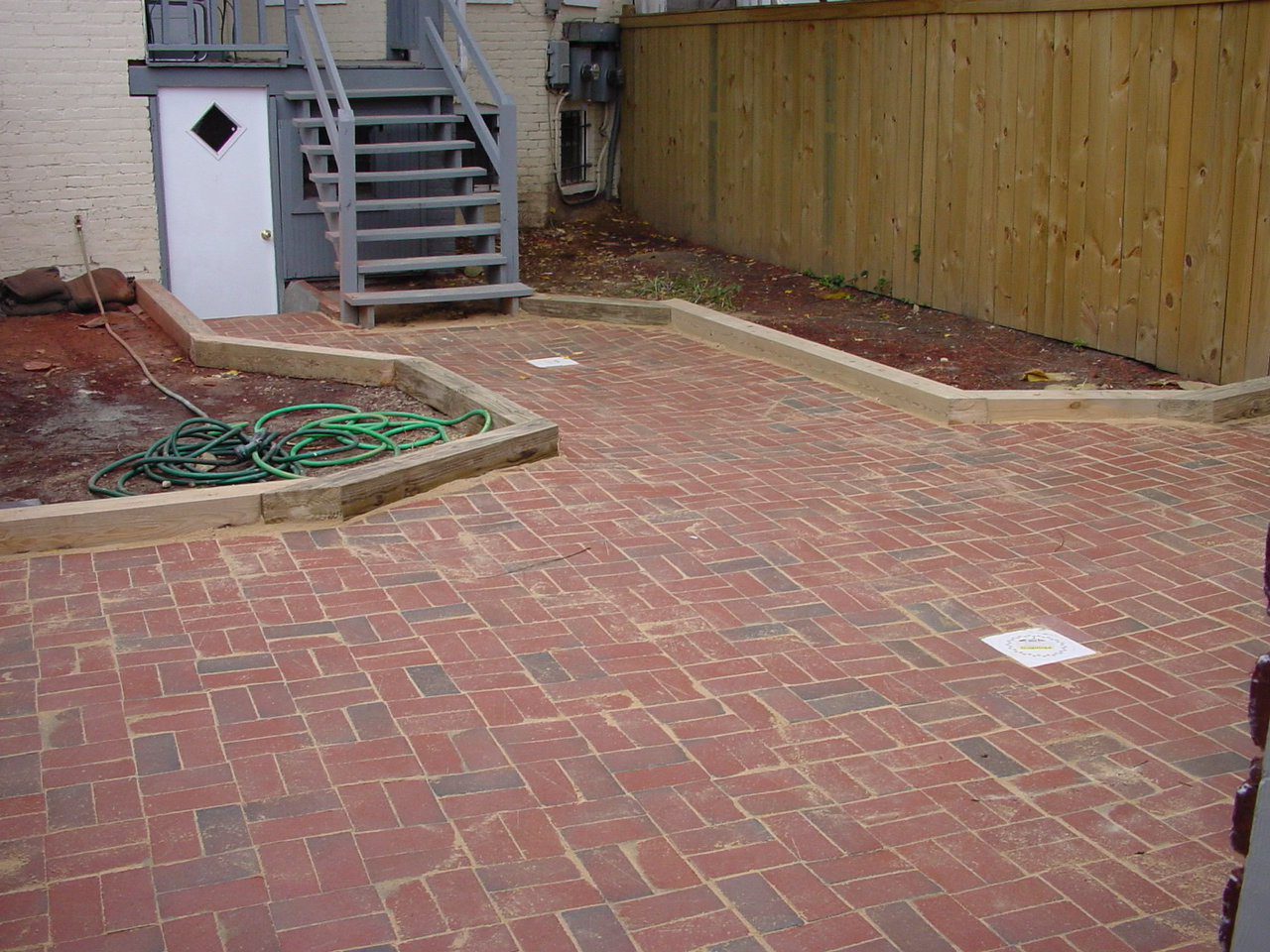 A backyard with red brick paving and a wooden fence.