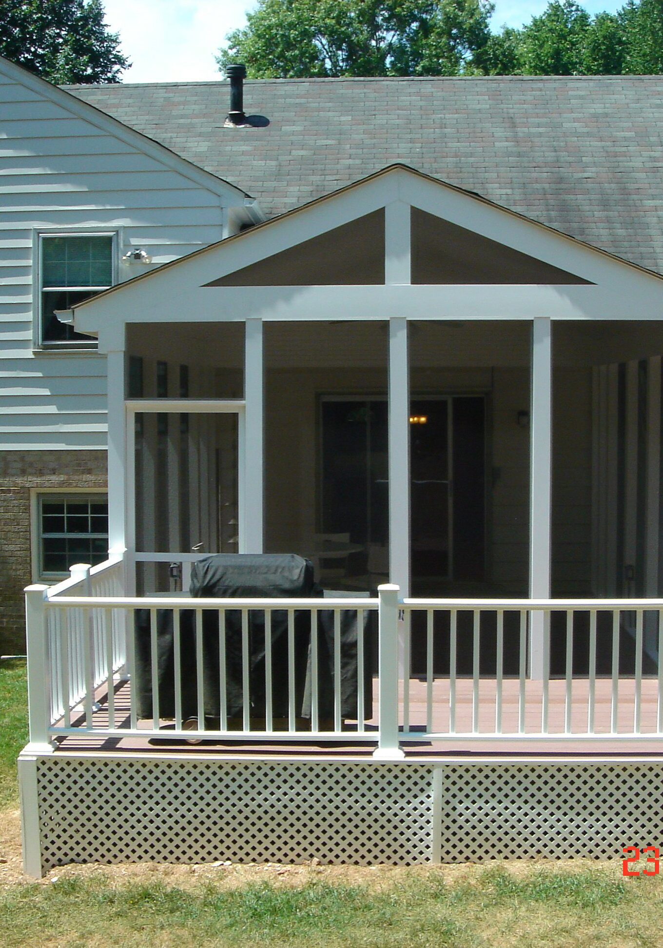 A small screened porch attached to a house with white railings and a gray roof.
